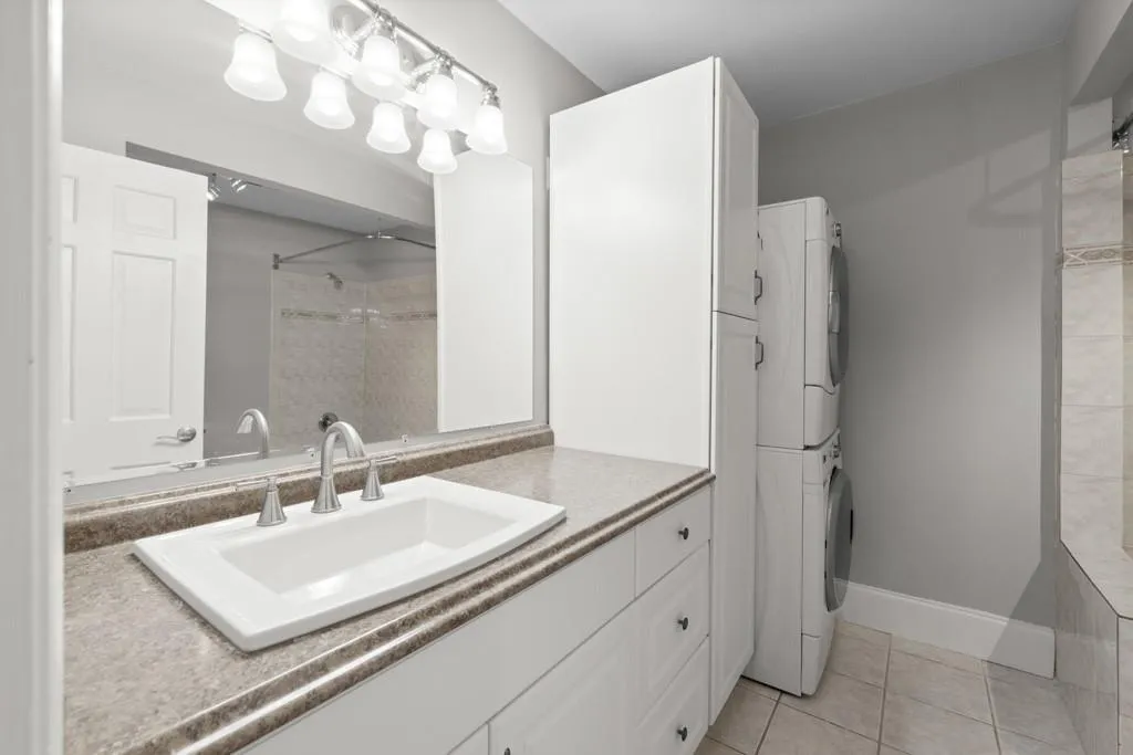 Bathroom with tiled shower, tile patterned flooring, stacked washing maching and dryer, and vanity