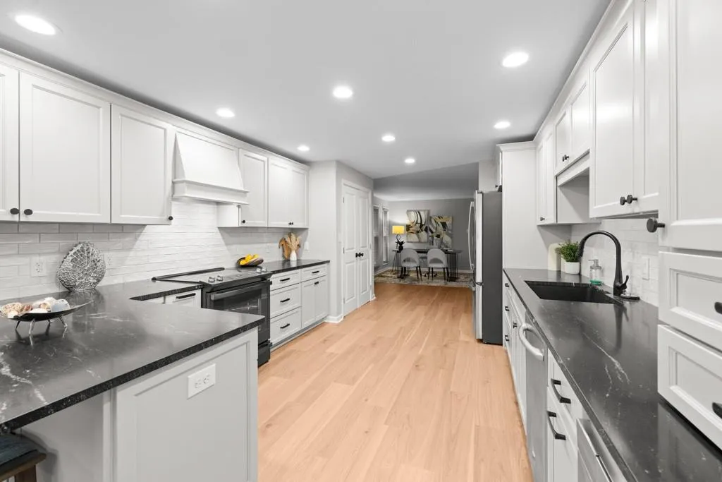Kitchen featuring custom range hood, sink, appliances with stainless steel finishes, and white cabinets