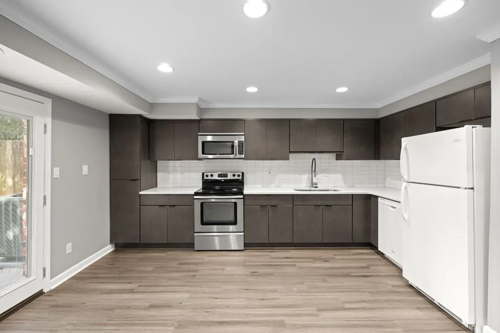 Kitchen featuring dark brown cabinets, crown molding, stainless steel appliances, sink, and light wood-type flooring