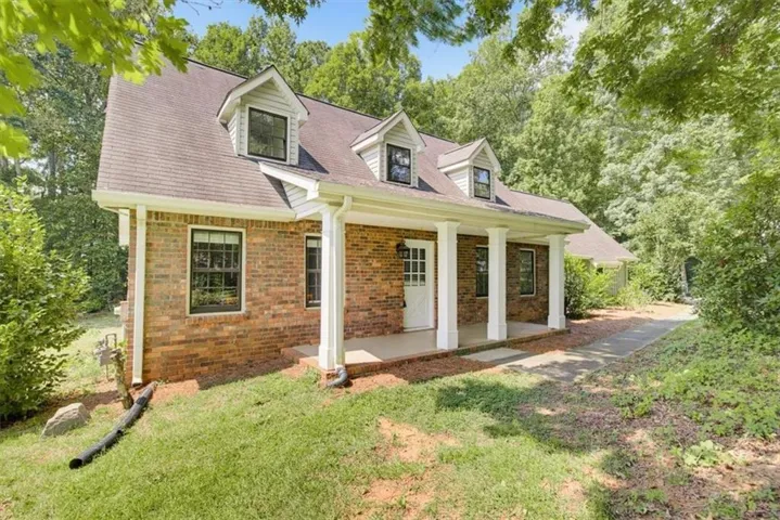 Brick exterior with multiple dormer windows, a covered front porch, and a paved walkway