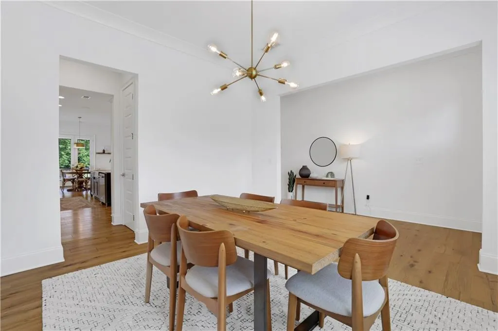 Spacious dining area featuring warm wood-finish flooring, crisp white walls, and an overhead sputnik chandelier