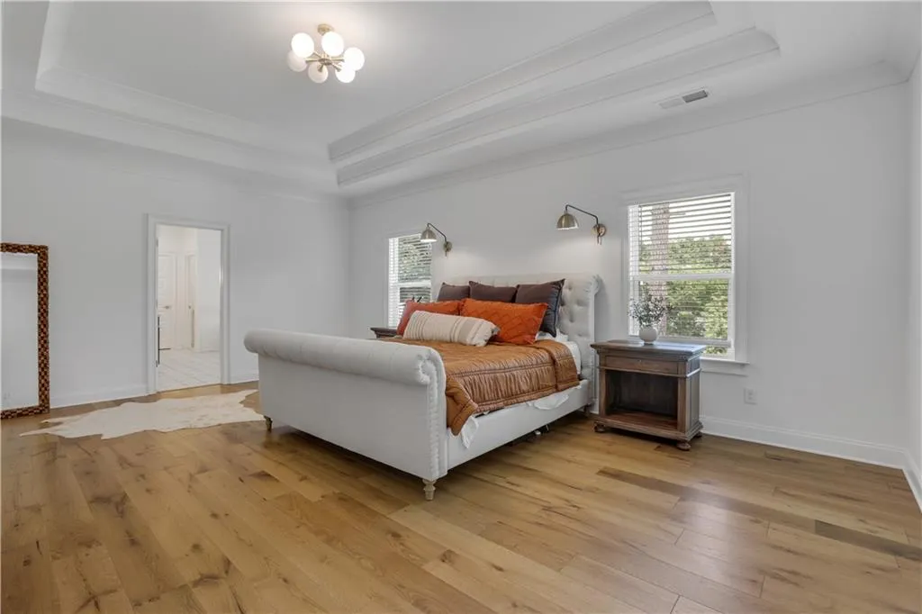 Expansive room featuring wood-finish flooring, a tray ceiling with crown molding, and a modern globe chandelier
