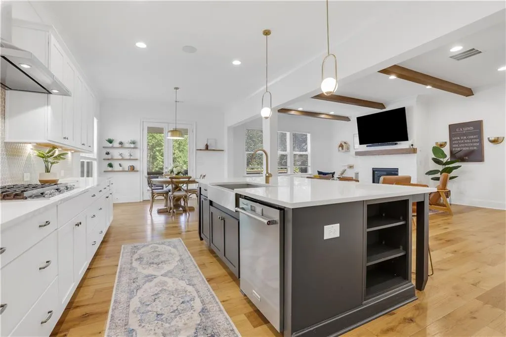 Open-concept kitchen featuring an oversized island with a farmhouse sink, white perimeter cabinetry, stainless steel appliances, and wood-finish flooring