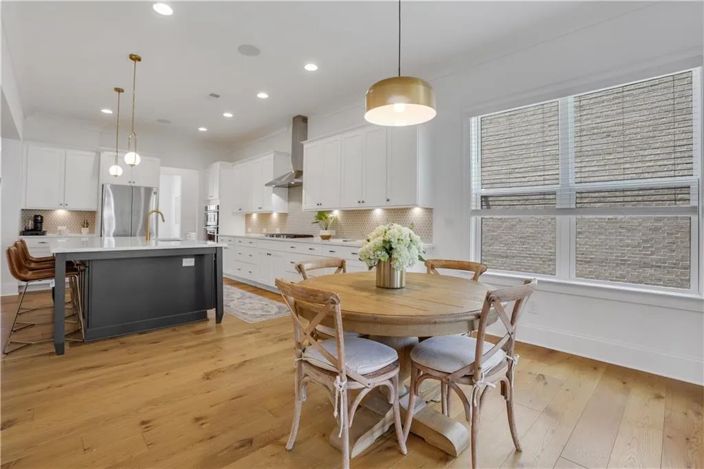 Open-concept kitchen with wood-finish flooring, white cabinetry, a dark-toned island with seating, a stainless steel range hood, and recessed lighting