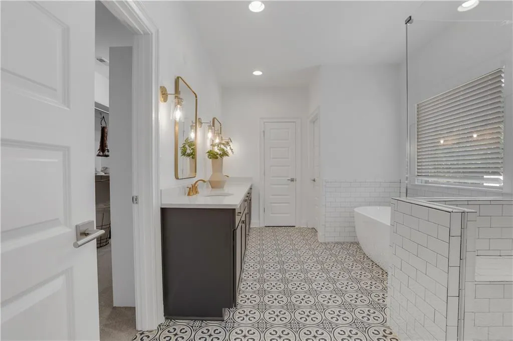 Spacious bathroom featuring patterned tile flooring, a dual-sink vanity with gold-tone fixtures, a freestanding bathtub, and a tiled shower enclosure