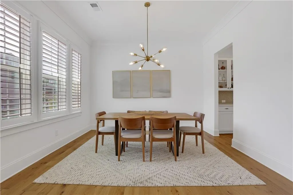 Spacious dining area featuring wood-finish flooring, a contemporary sputnik chandelier, white plantation shutters on multiple windows, and crown molding
