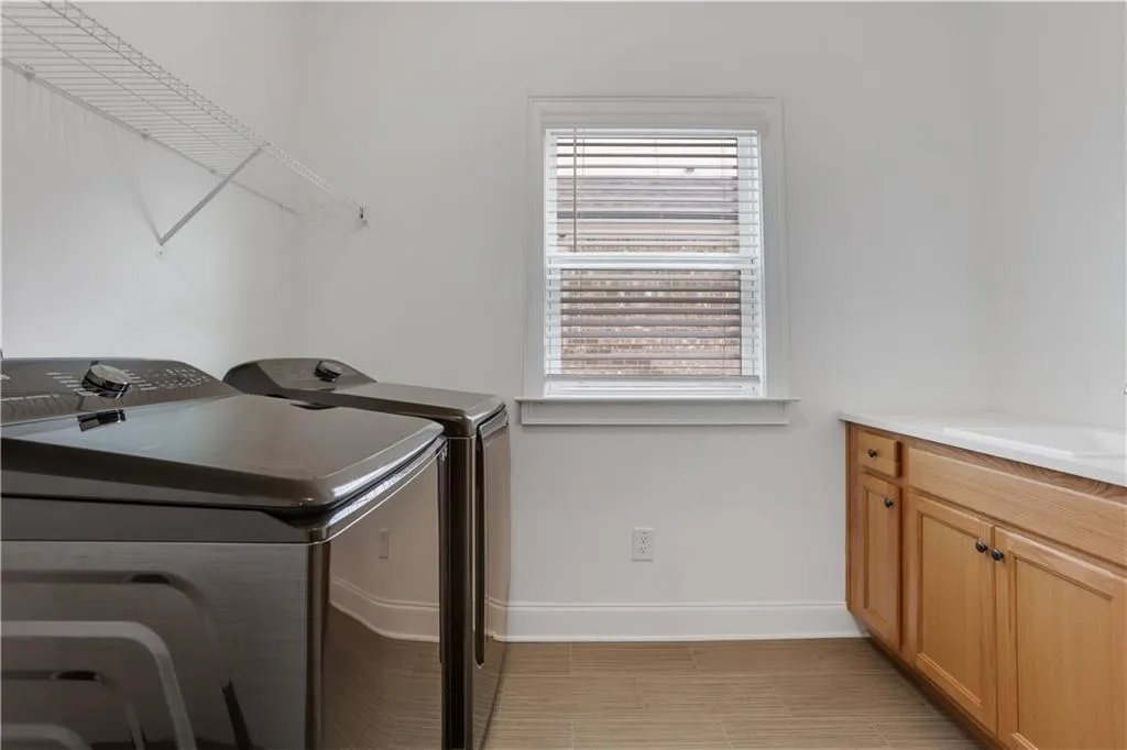 Utility room featuring light wood-finish cabinetry with dark hardware, a white countertop, a single-pane window with blinds, and light-toned tile flooring