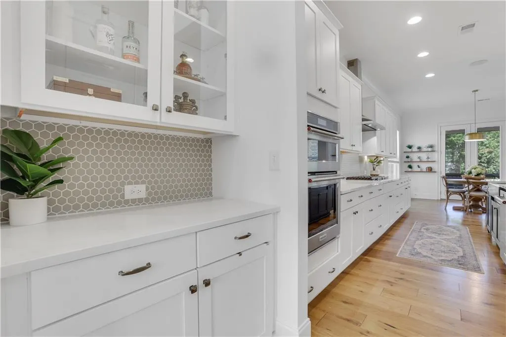Gourmet kitchen featuring white shaker cabinetry, stainless steel double ovens, a hexagon tile backsplash, light wood-finish flooring, and recessed ceiling lighting