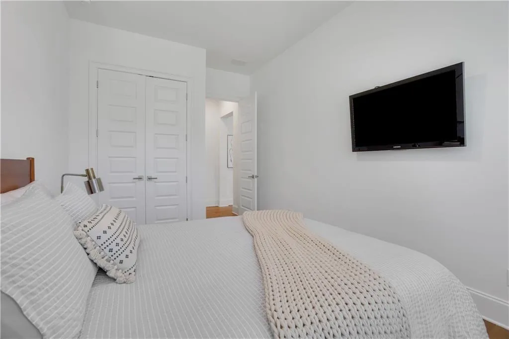 Bedroom featuring light wood flooring, white walls, and a built-in wall-mounted television
