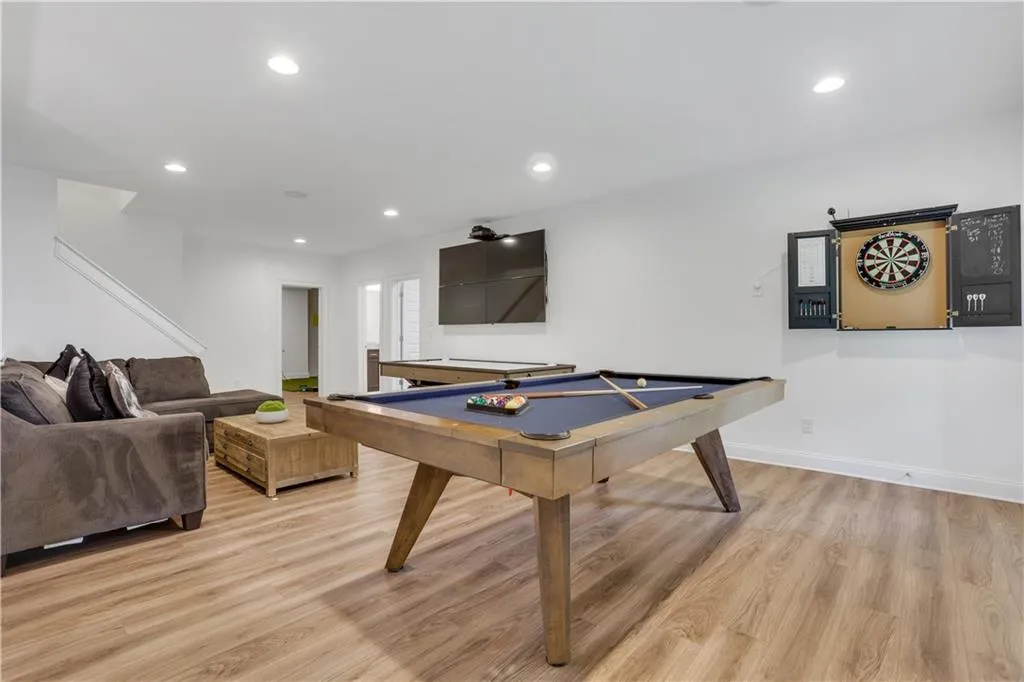 Expansive recreational space featuring light wood-finish flooring, recessed lighting, and a built-in dartboard cabinet