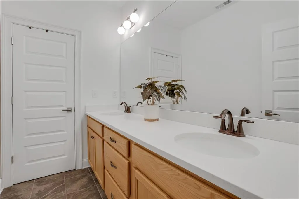 Bathroom featuring a dual vanity with light wood cabinetry, white countertops, two integrated sinks, and bronze-finish faucets