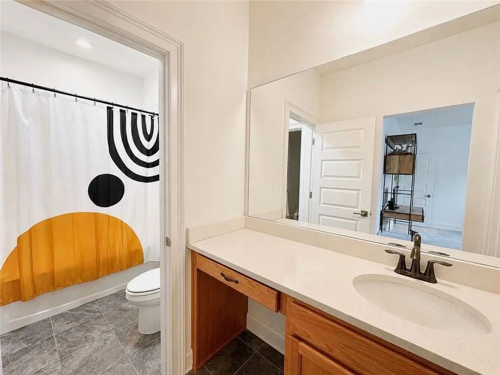 Bathroom vanity featuring a light-toned countertop, undermount sink with bronze-finish fixtures, and integrated wood-finish cabinetry