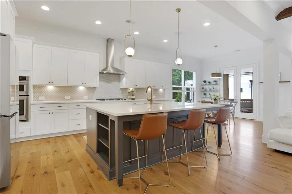 Gourmet kitchen featuring a large central island, light wood-finish flooring, white cabinetry, integrated stainless steel appliances, and French doors