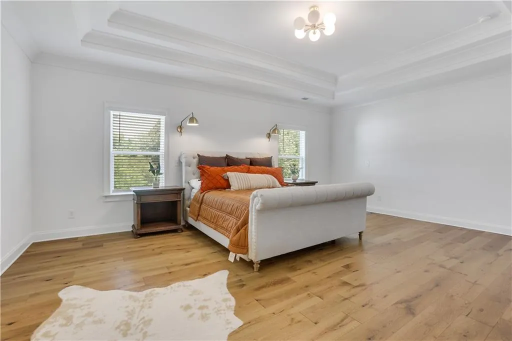 Spacious room featuring wood-finish flooring, a contemporary ceiling light fixture, and a layered tray ceiling