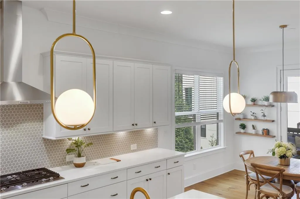 Kitchen featuring white shaker cabinetry, white countertops, a stainless steel range hood, hexagonal tile backsplash, and golden pendant lighting