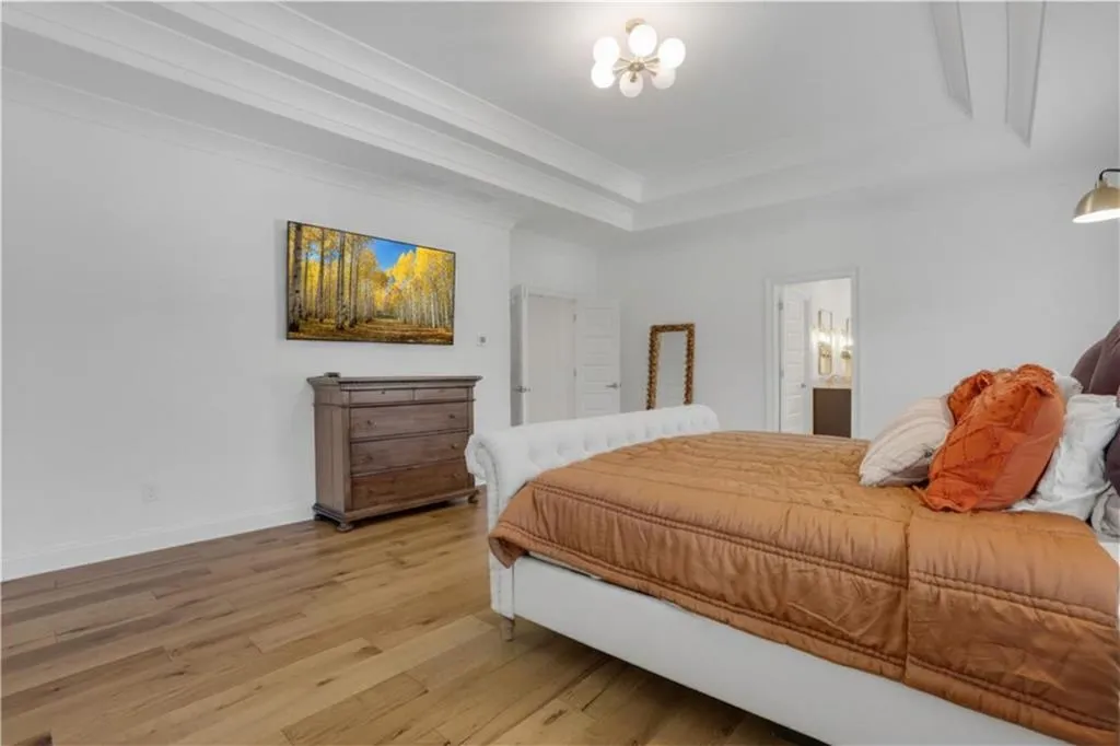 Spacious room featuring wood-finish flooring, white walls, and a multi-tiered tray ceiling