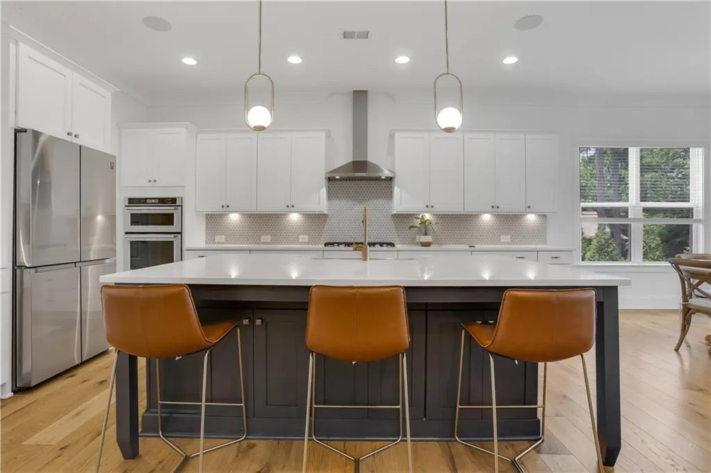 Spacious kitchen featuring an expansive center island with seating, stainless steel appliances, white cabinetry, and wood-finish flooring