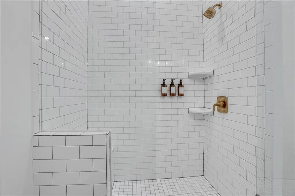 Shower enclosure featuring white subway tile, a built-in bench, two corner shelves, and a bronze-finish showerhead and controls