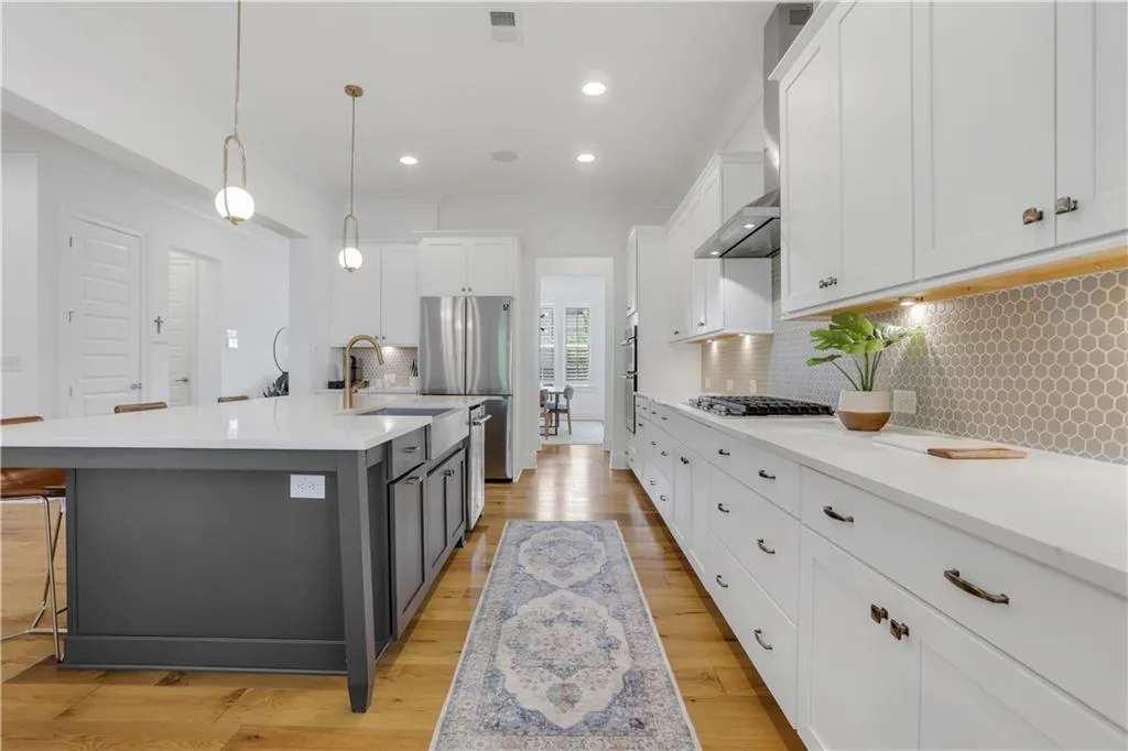 Gourmet kitchen with a large central island, white shaker cabinetry, stainless steel appliances, and wood-finish flooring