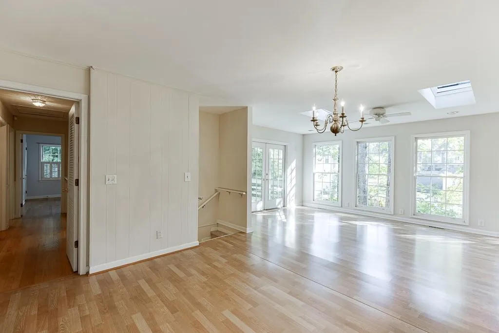 Unfurnished dining area featuring an inviting chandelier, a skylight, light wood-type flooring, and baseboards