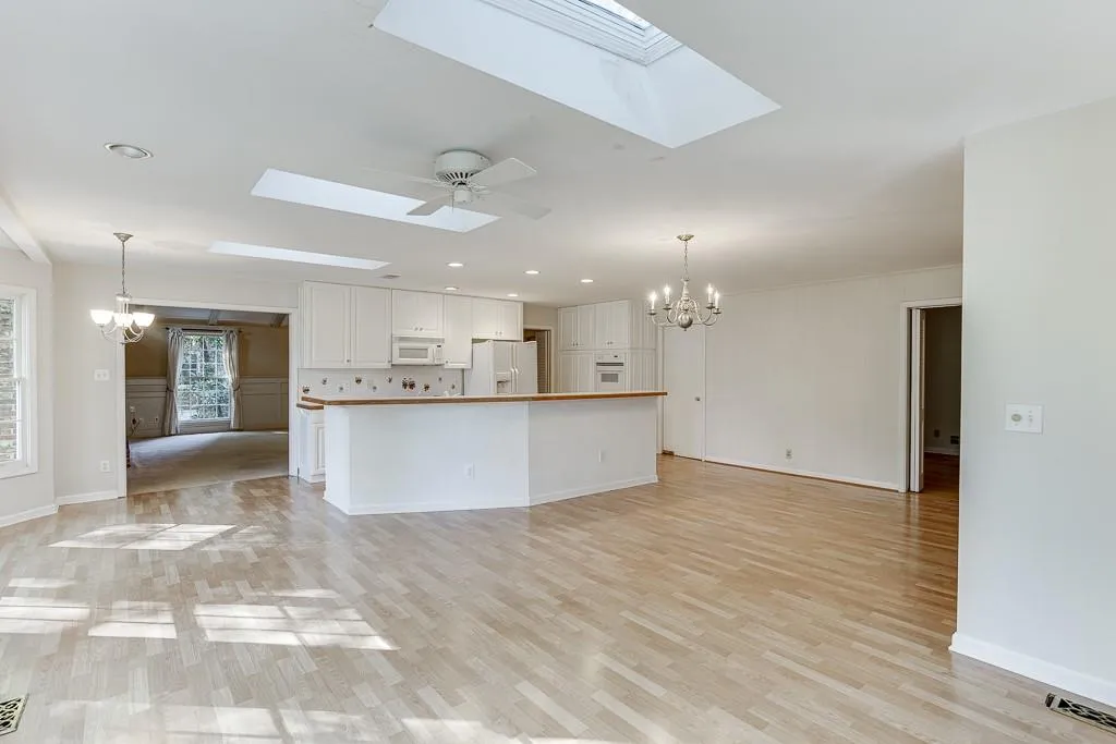 Kitchen with white appliances, white cabinetry, a skylight, and ceiling fan with notable chandelier