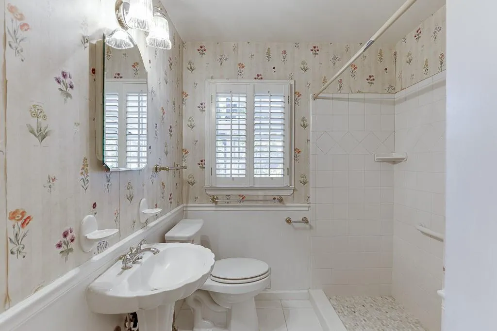 Bathroom with tiled shower, wallpapered walls, a sink, tile patterned floors, and toilet