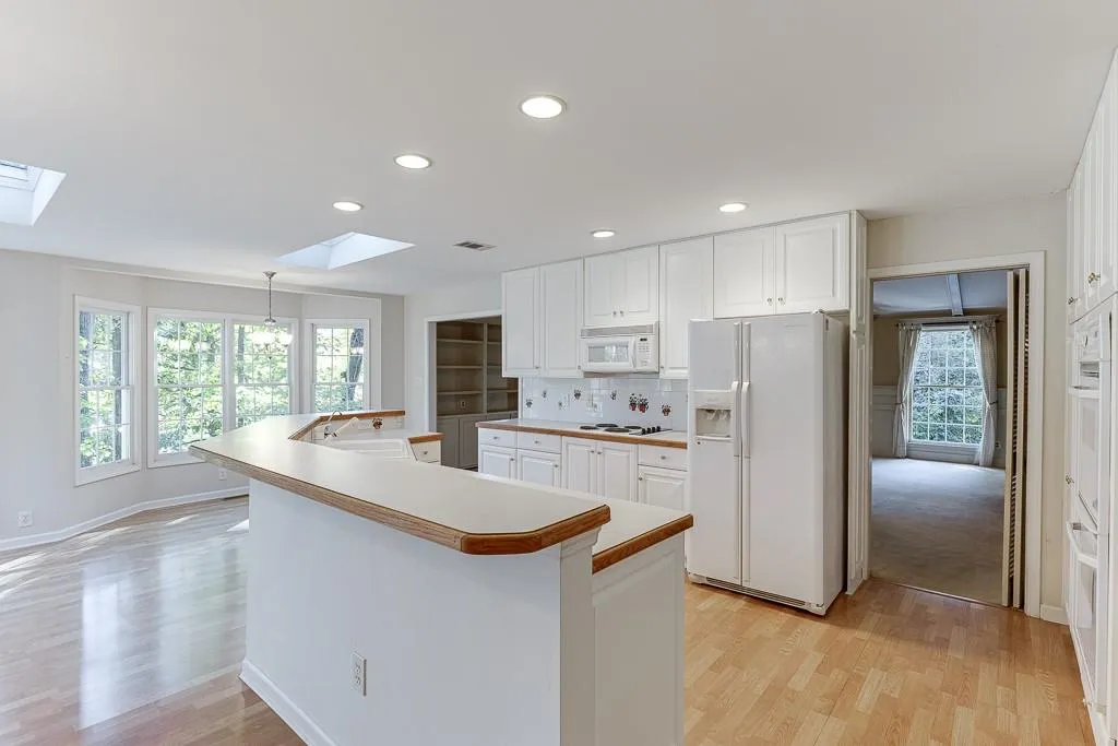 Kitchen featuring white cabinetry, white appliances, a skylight, and light wood-type flooring