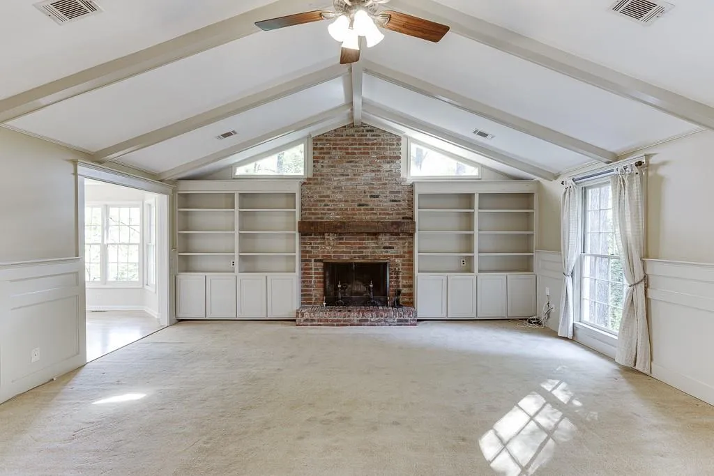 Unfurnished living room with visible vents, wainscoting, built in shelves, and vaulted ceiling with beams