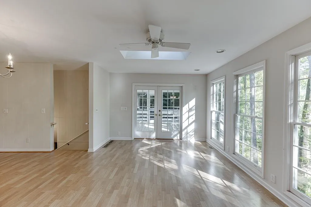 Unfurnished room featuring visible skylights, french doors, light wood finished floors, baseboards, and ceiling fan