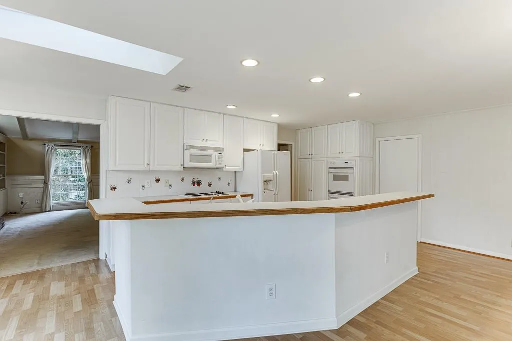 Kitchen featuring visible vents, white appliances, a skylight, and white cabinets
