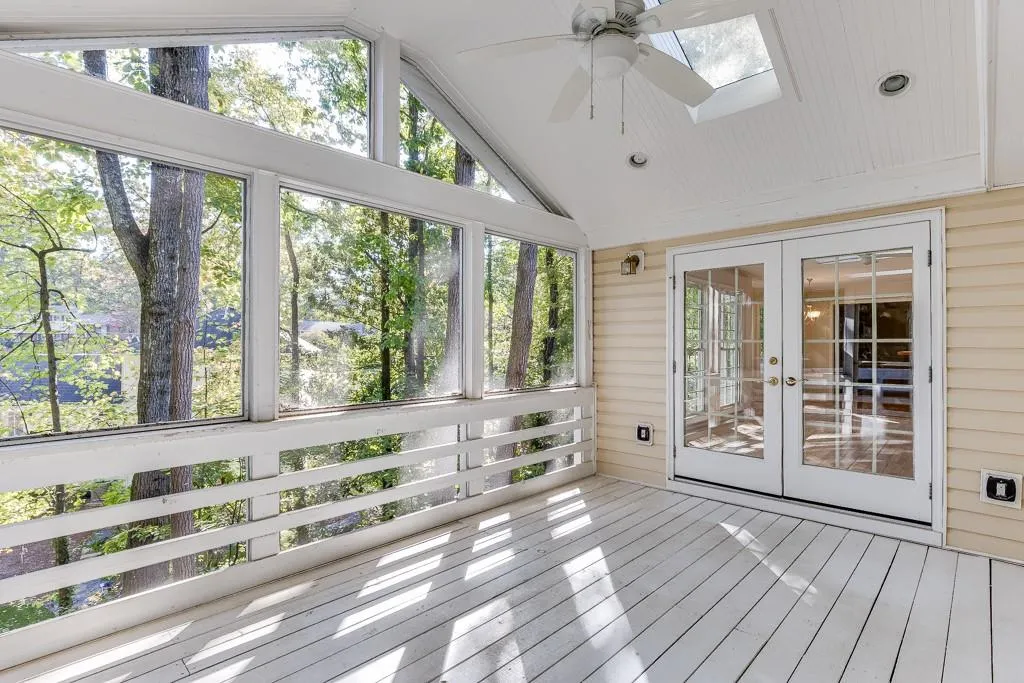 Unfurnished sunroom featuring a ceiling fan, vaulted ceiling with skylight, and french doors