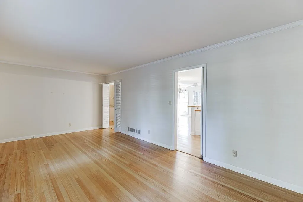Empty room with visible vents, baseboards, light wood-style floors, and ornamental molding