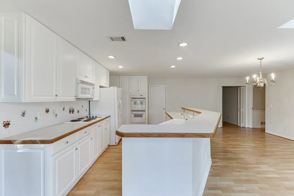 Kitchen featuring light wood-type flooring, visible vents, white appliances, a skylight, and white cabinets