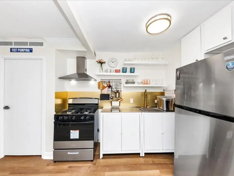 Kitchen with stainless steel appliances, white cabinets, open shelves, light wood finished floors, and beamed ceiling