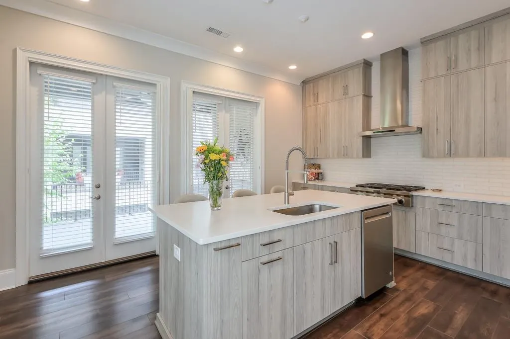 Kitchen featuring range hood, a kitchen island with sink and dishwasher, and an abundance of natural light