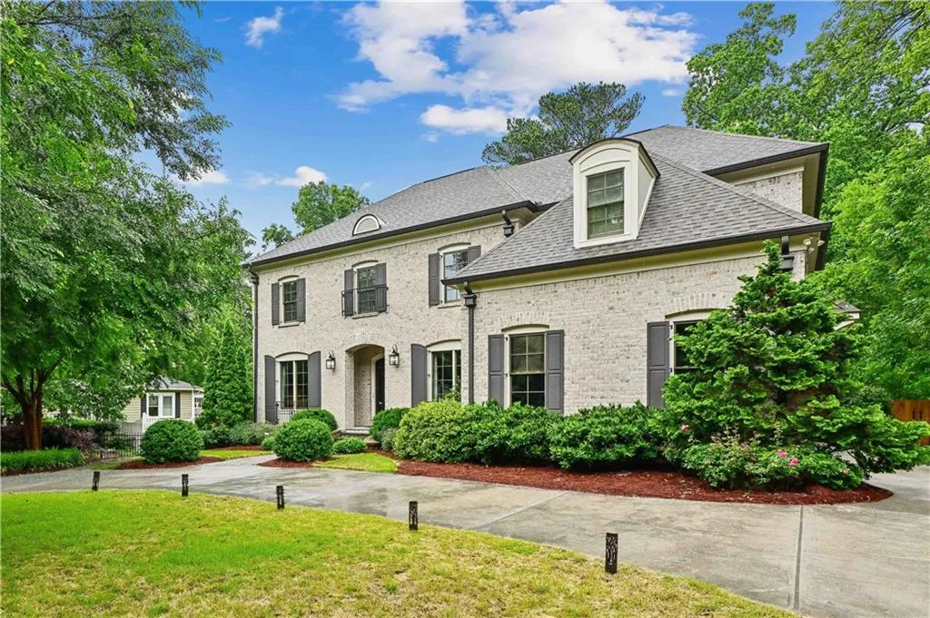 French country inspired facade featuring a front lawn, a shingled roof, and brick siding