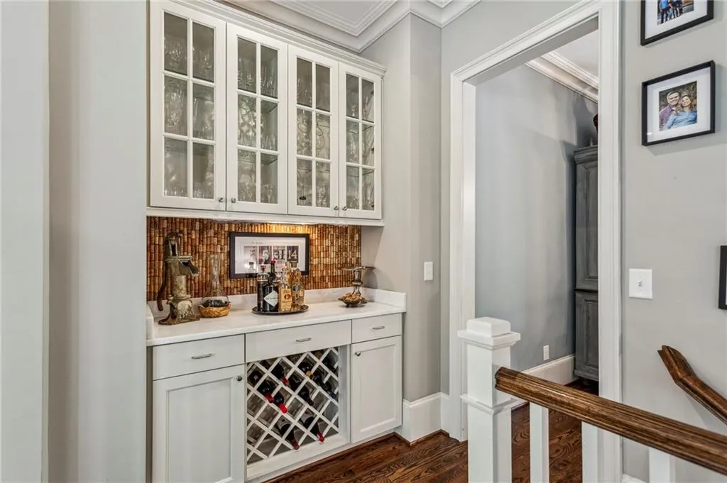 Indoor dry bar featuring ornamental molding, dark wood-style flooring, decorative backsplash, and baseboards