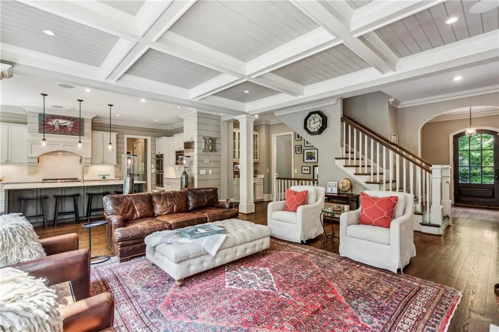 Living area featuring dark wood-type flooring, beam ceiling, decorative columns, stairway, and coffered ceiling