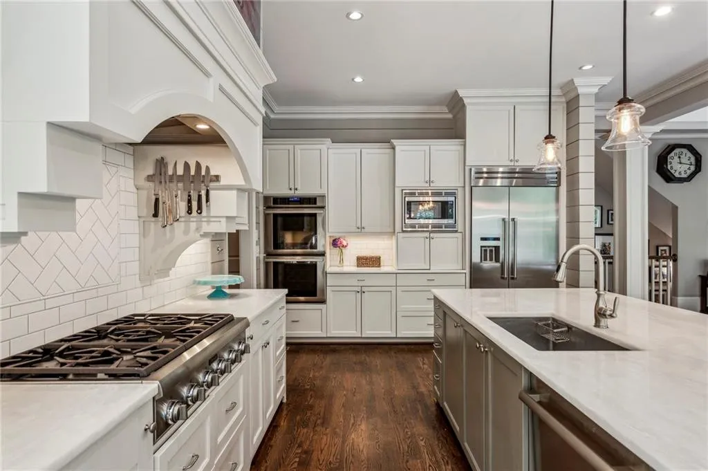 Kitchen with built in appliances, a sink, ornamental molding, hanging light fixtures, and white cabinets