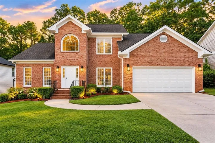Brick exterior with white trim, arched window, two-car garage, and established landscaping