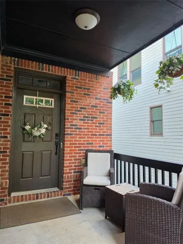 Covered porch featuring a brick facade and dark wood door with transom
