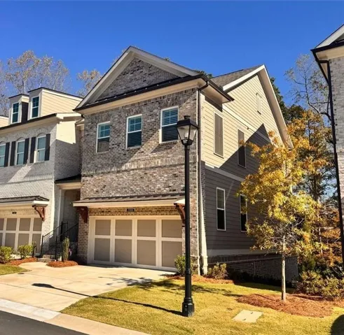 Brick and siding exterior, two-car garage, concrete driveway, front yard with mature trees, and a streetlamp