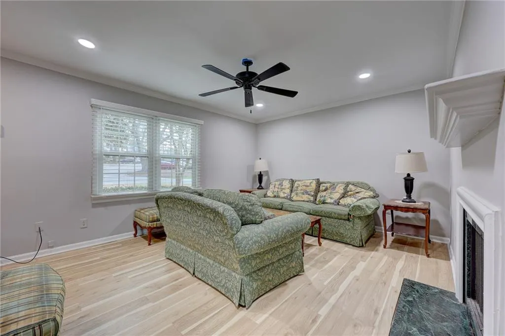 Living area featuring light wood-type flooring, ornamental molding, a fireplace with flush hearth, ceiling fan, and recessed lighting