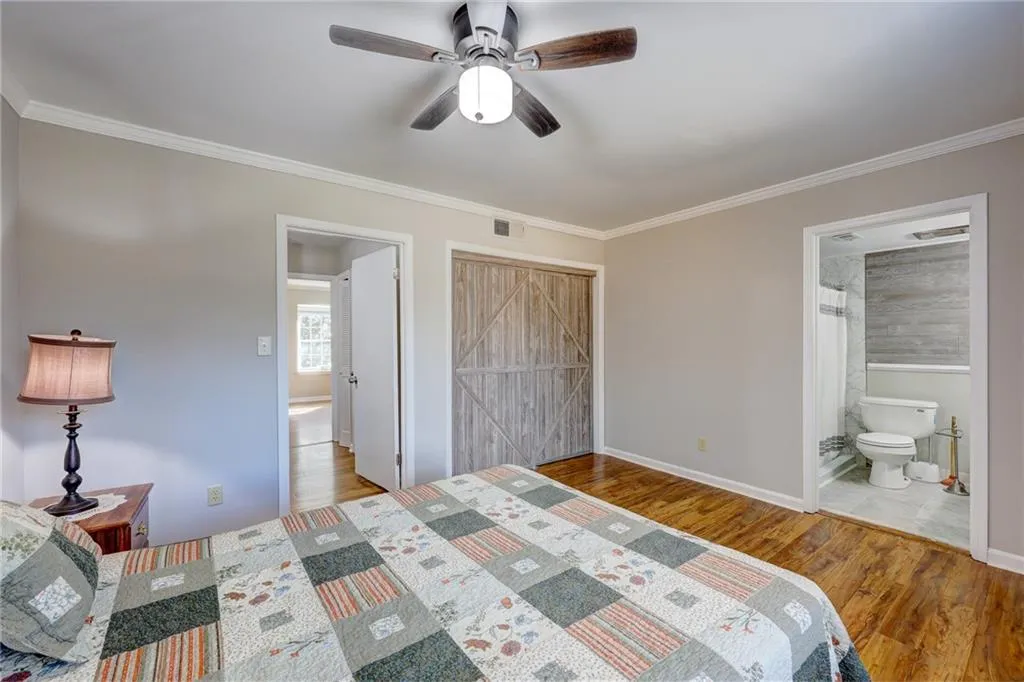 Bedroom featuring ensuite bath, a closet, light wood-type flooring, ornamental molding, and a ceiling fan