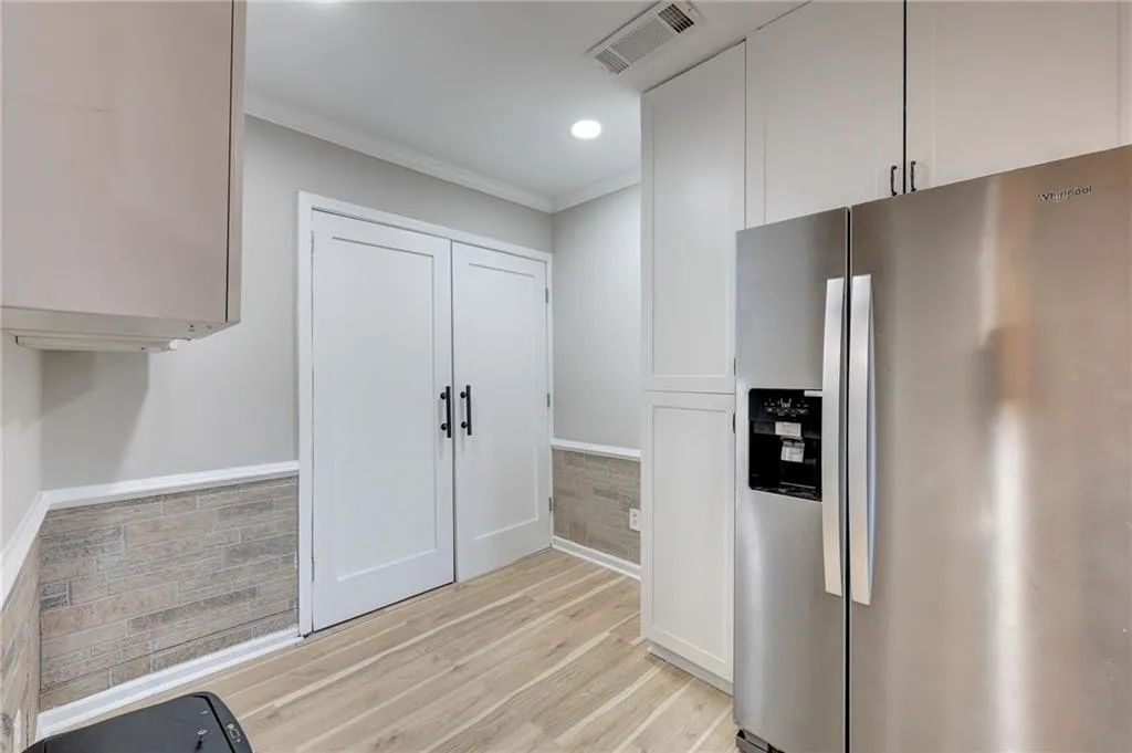 Kitchen featuring stainless steel fridge, ornamental molding, light wood finished floors, white cabinets, and recessed lighting