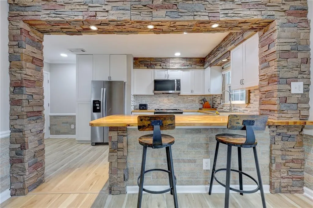 Kitchen featuring butcher block countertops, stainless steel appliances, a peninsula, white cabinetry, and light wood-style flooring
