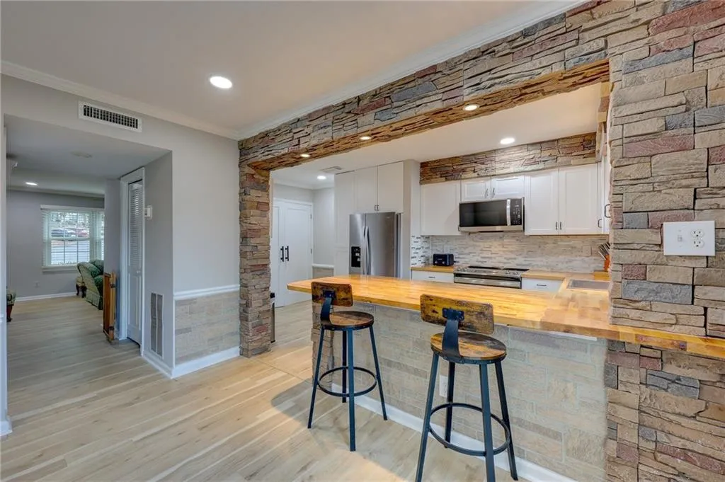 Kitchen featuring white cabinets, a peninsula, a kitchen bar, crown molding, and wooden counters