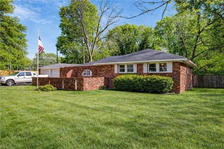 Brick exterior residence featuring a dark shingle roof, white window shutters, and a well-maintained front lawn