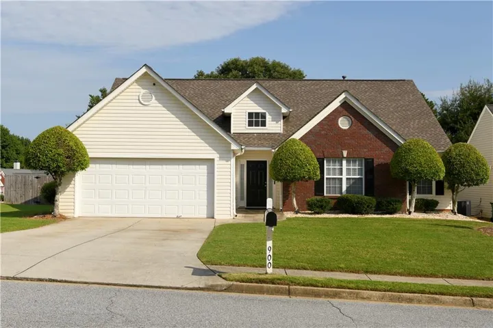 Traditional-style home featuring a two-car garage, brick facade detailing, and a shingled roof