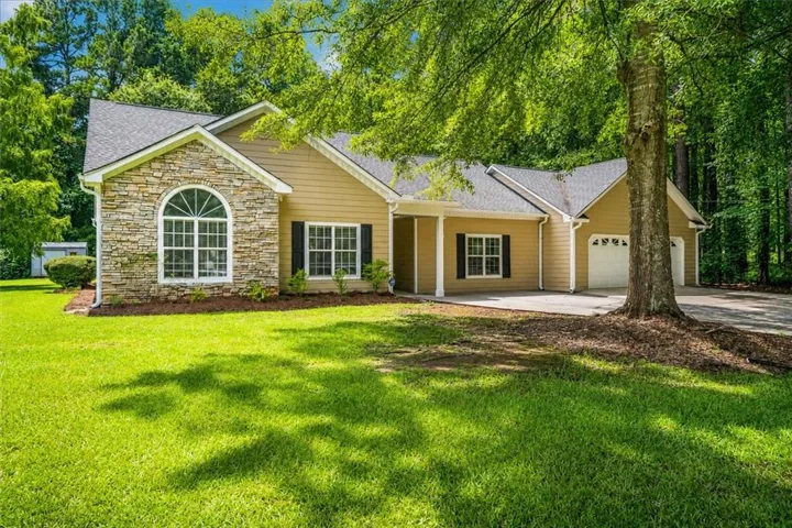 Stone facade home featuring a prominent arched window, tan siding, dark shutters, and an attached two-car garage